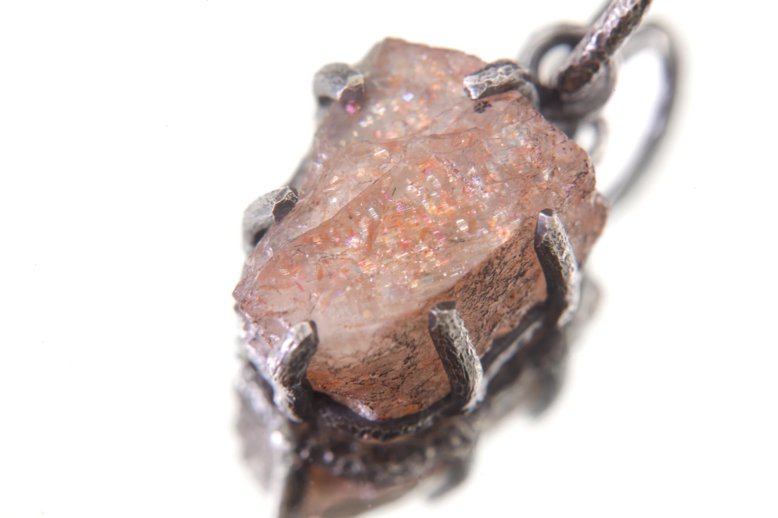 Raw Sunstone pendant on white background showing natural orange-brown gemstone and rugged oxidized silver claws.