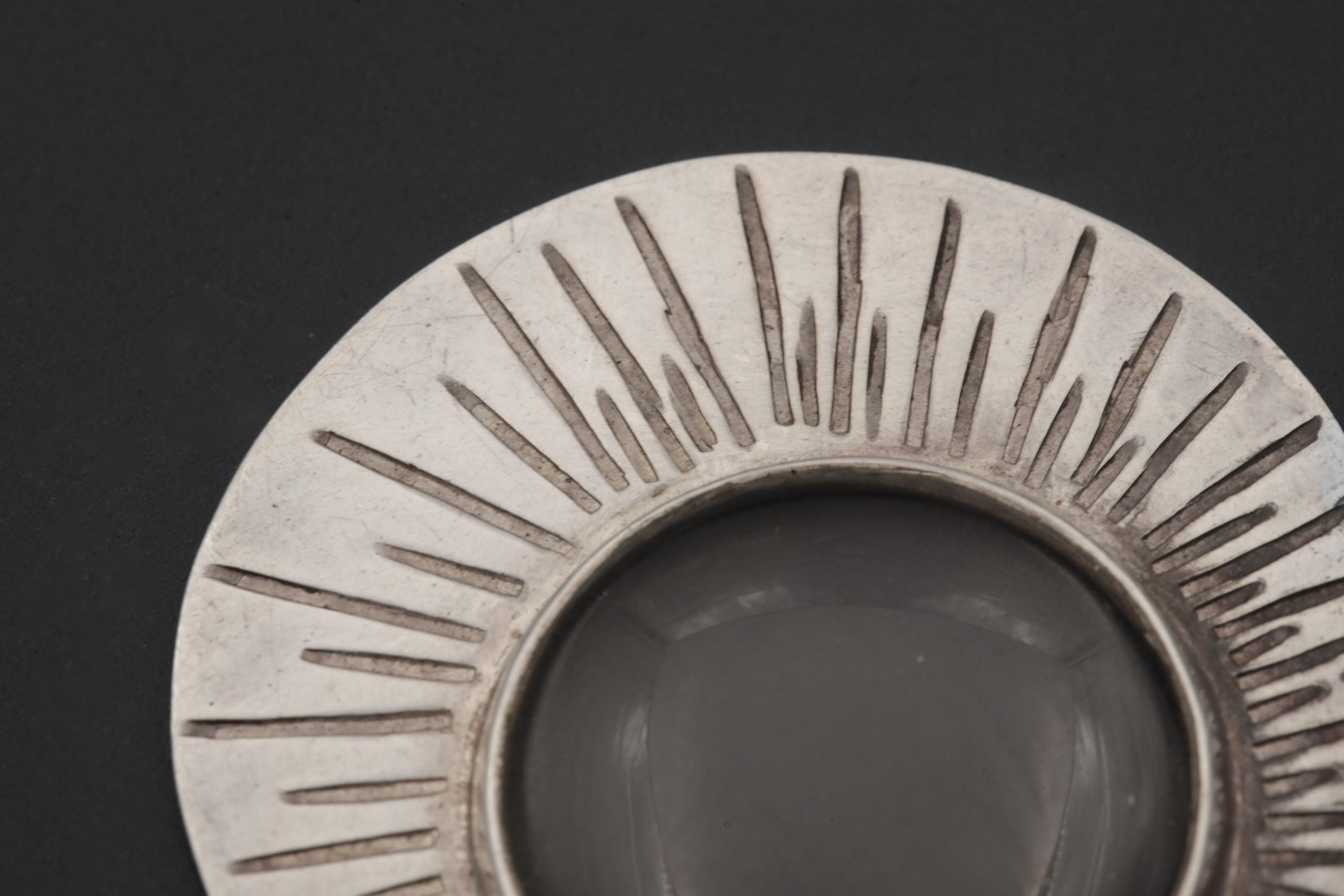 Close-up of Sun Motif pendant showing scratch-textured sterling silver rays and central magnifying glass lens.