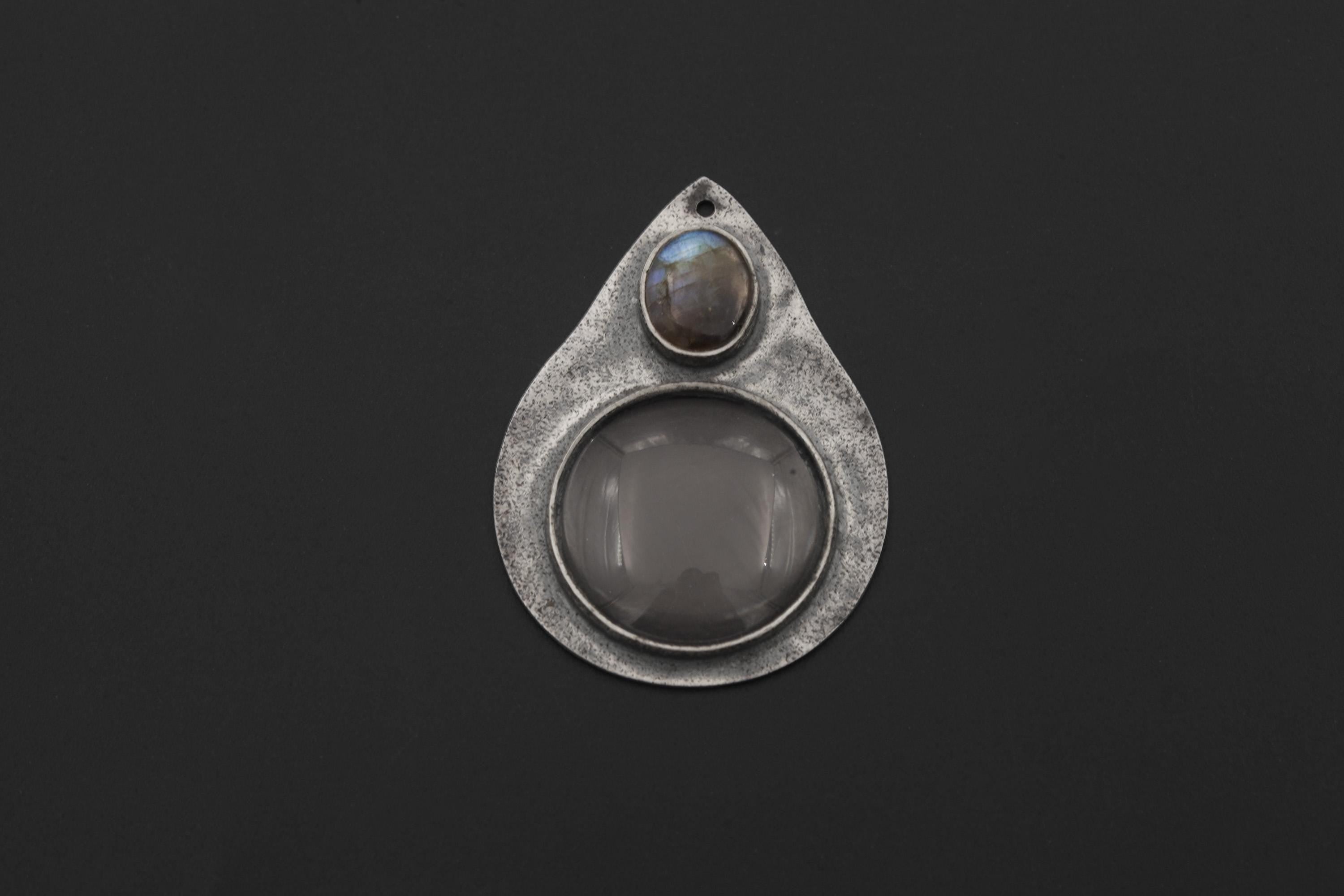 Labradorite magnifying glass pendant displayed on dark background with teardrop silver frame and optical lens.