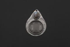 Labradorite magnifying glass pendant displayed on dark background with teardrop silver frame and optical lens.