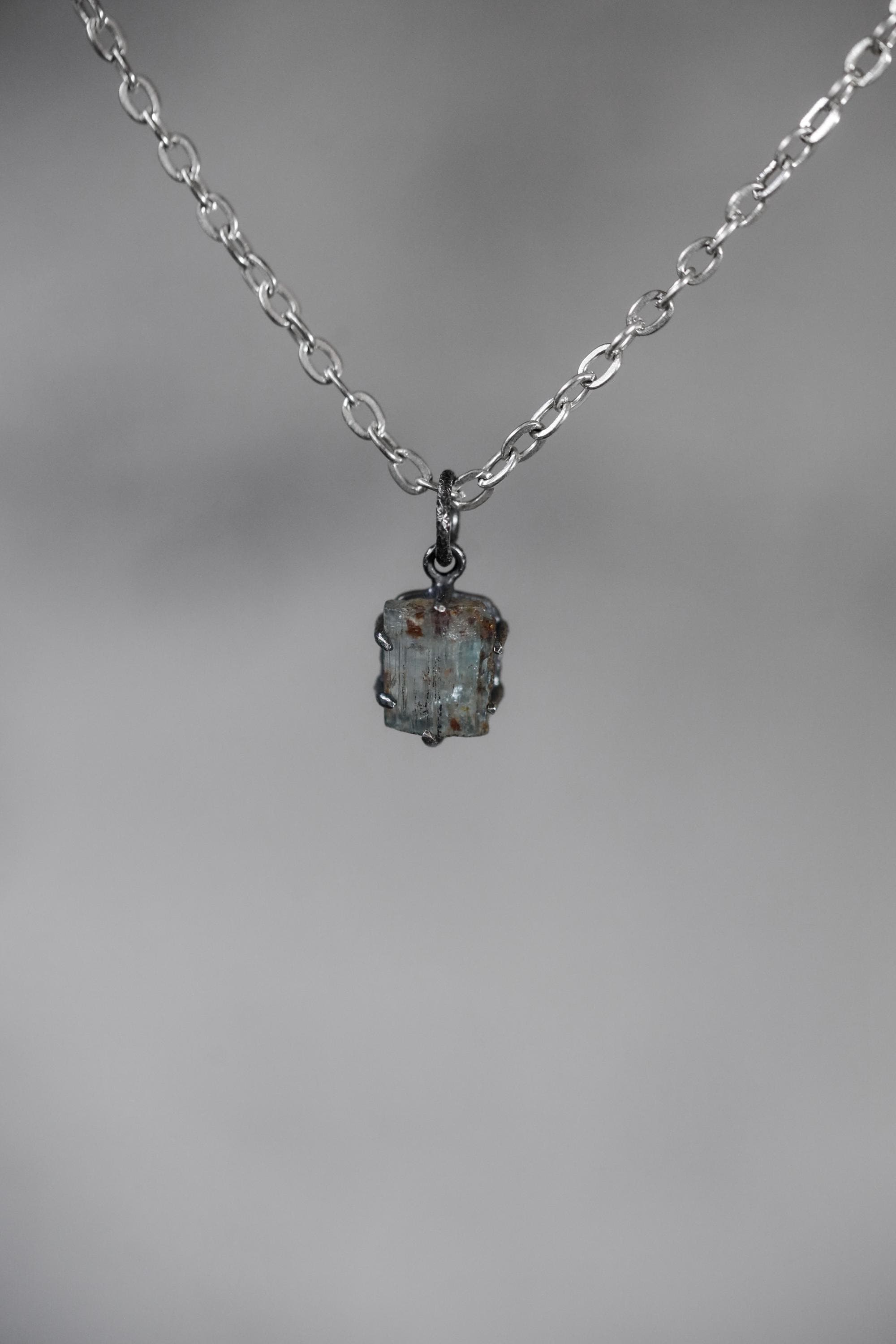 Australian Aquamarine pendant on grey background showing oxidized sterling silver claws and natural crystal striations.