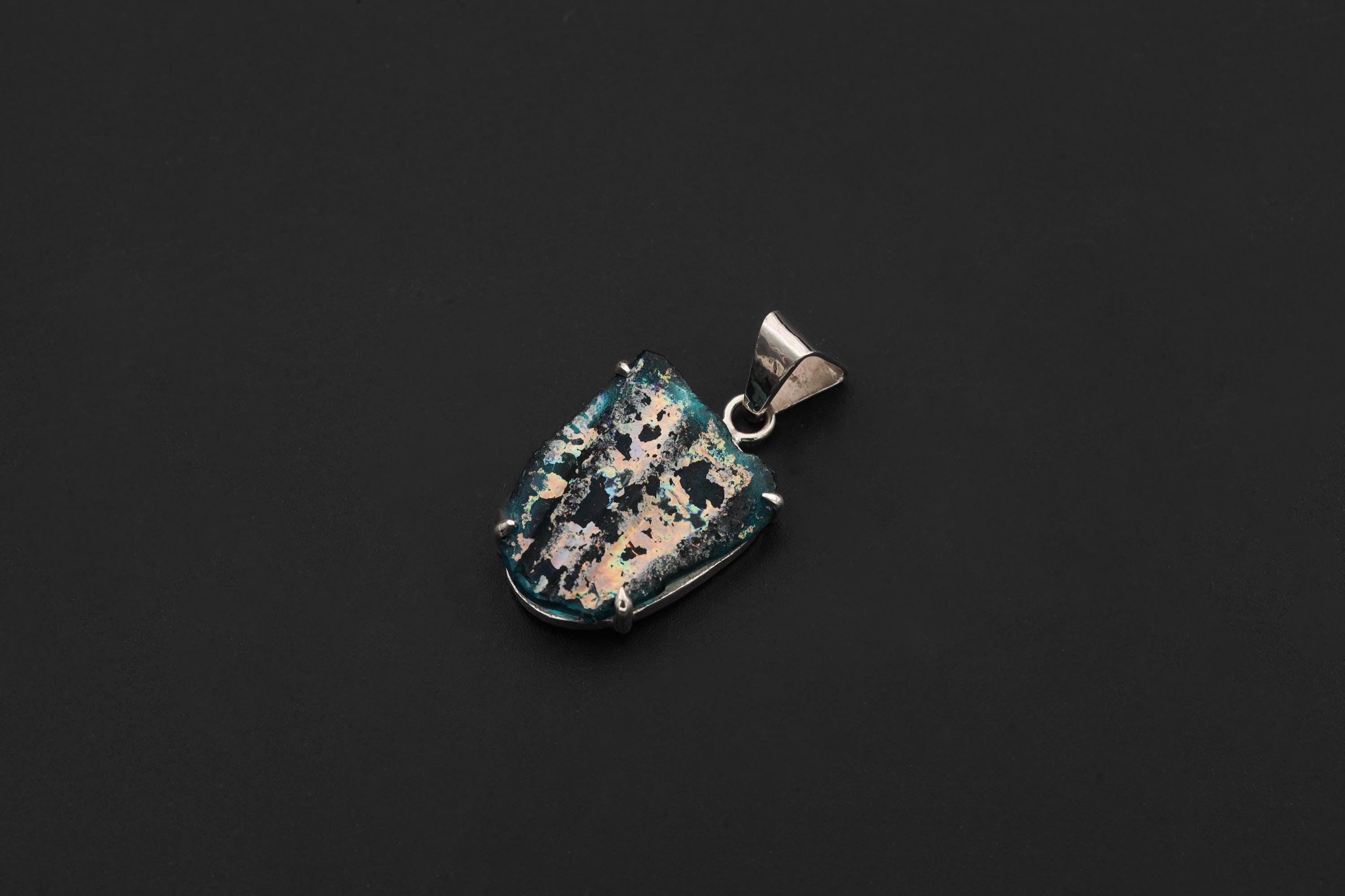 Ancient opalized glass pendant displayed on black background with claw-set sterling silver frame.