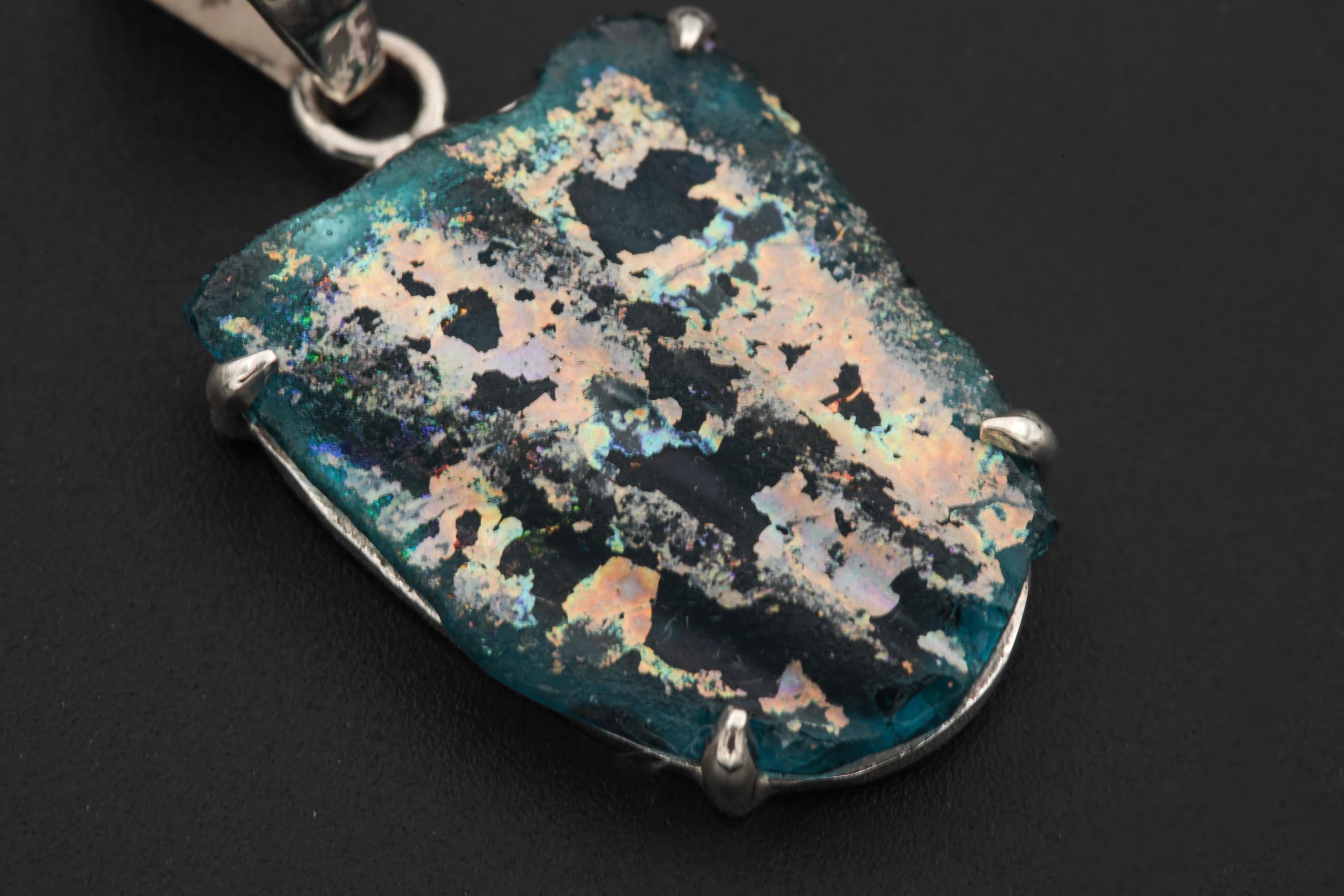 Close view of opalized glass pendant showing blue green gold iridescence and hammered silver bail.