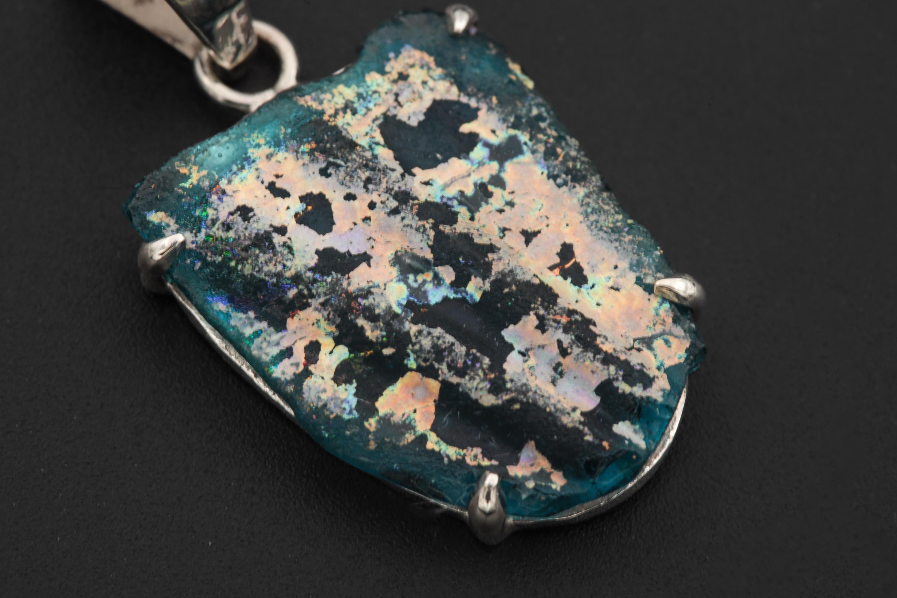 Close view of opalized glass pendant showing blue green gold iridescence and hammered silver bail.