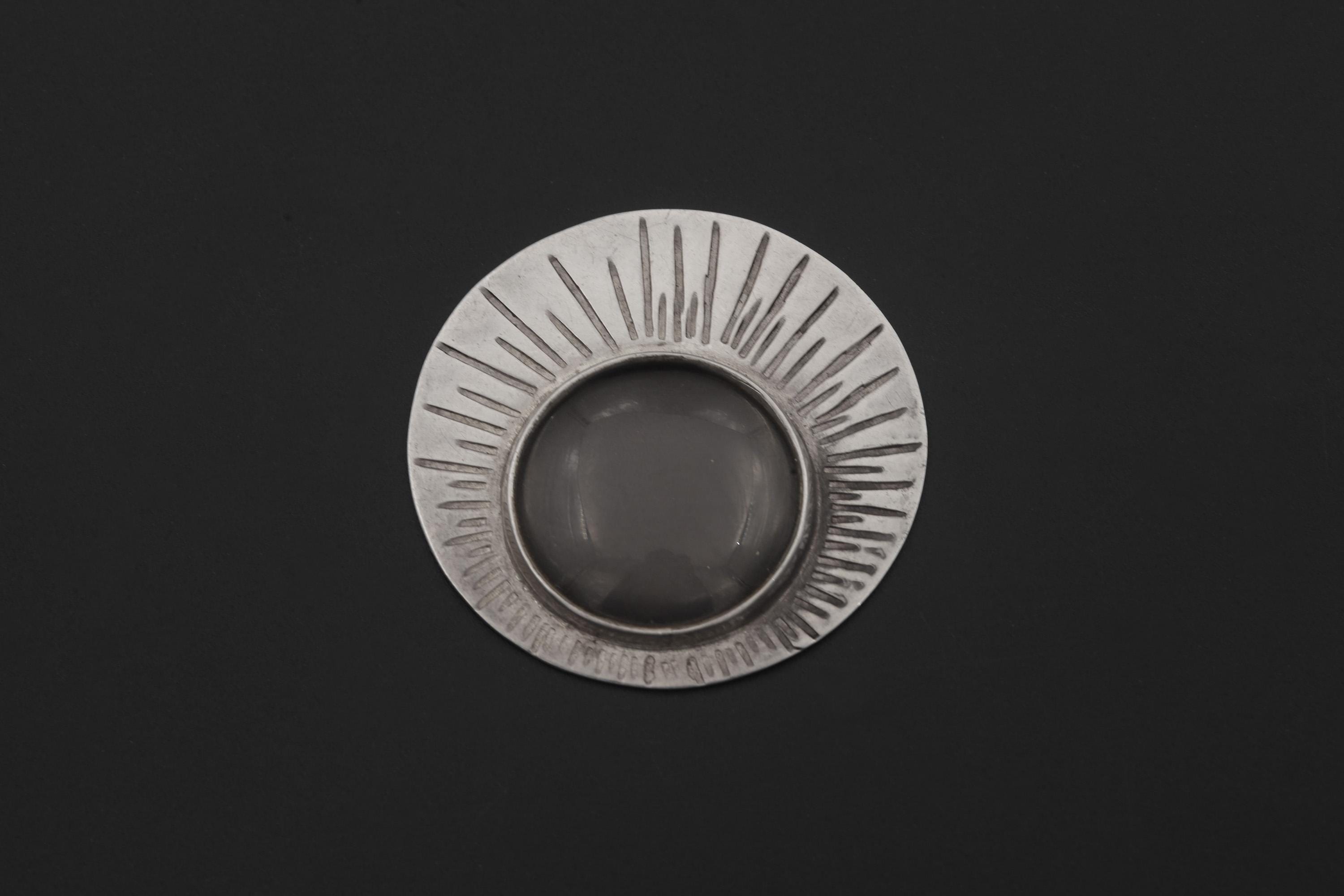 Sterling silver Sun magnifying glass pendant shown on dark background with central 5x optical lens.
