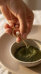South Sea Pearl gold-plated brass fairy spoon pendant shown being used with green powder in a small ceramic bowl.