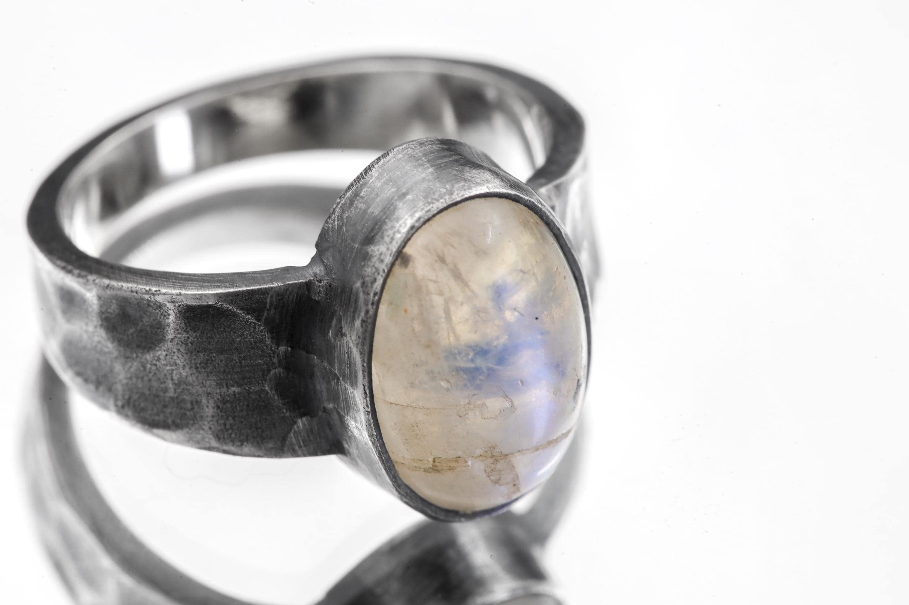 Close-up of AAA Blue Moonstone feldspar ring showing oval cabochon, oxidized silver bezel, and rugged hammered band.