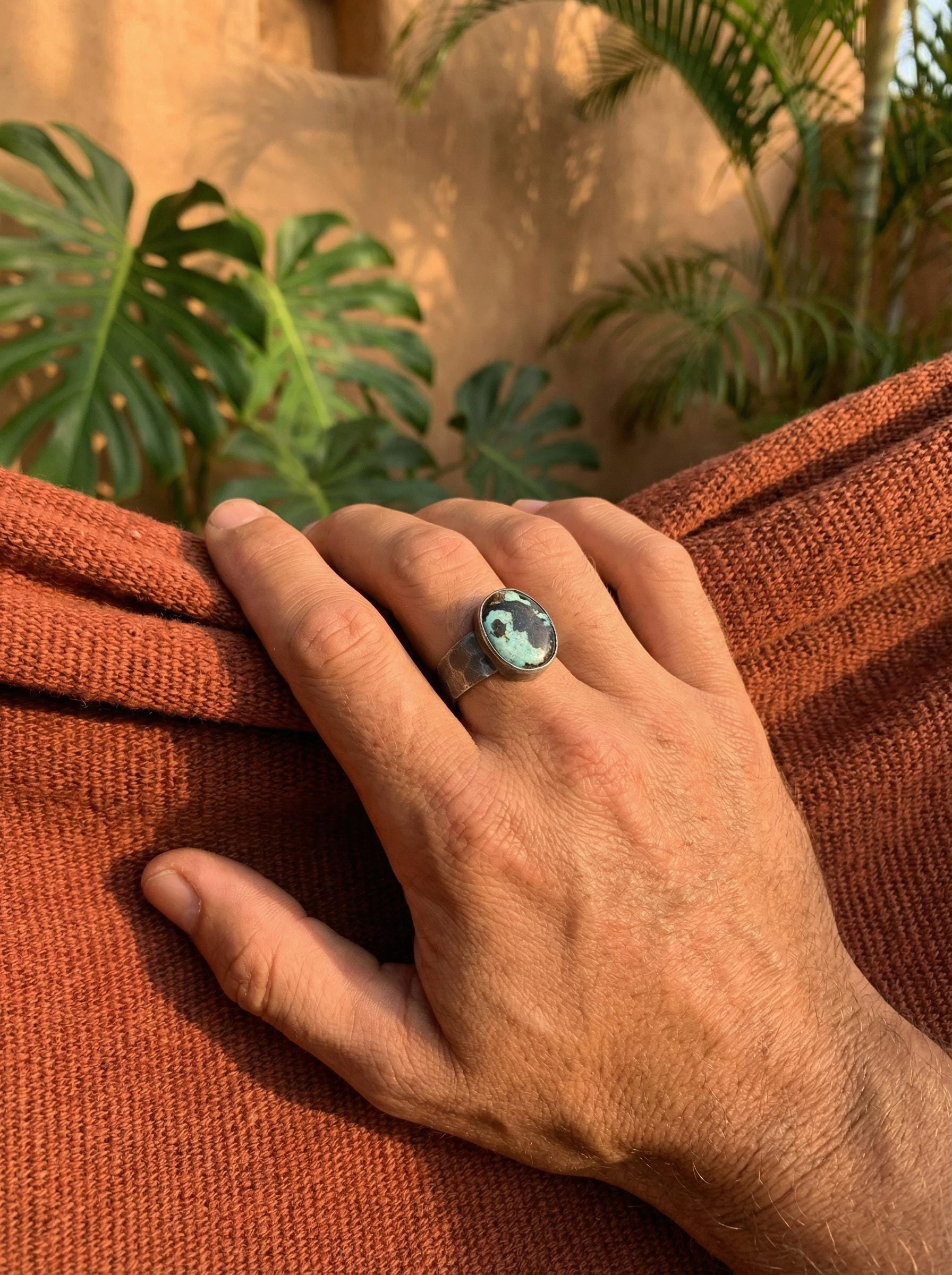 Tibetan Turquoise ring shown worn on the hand outdoors, with green matrix stone and rugged oxidized silver band.