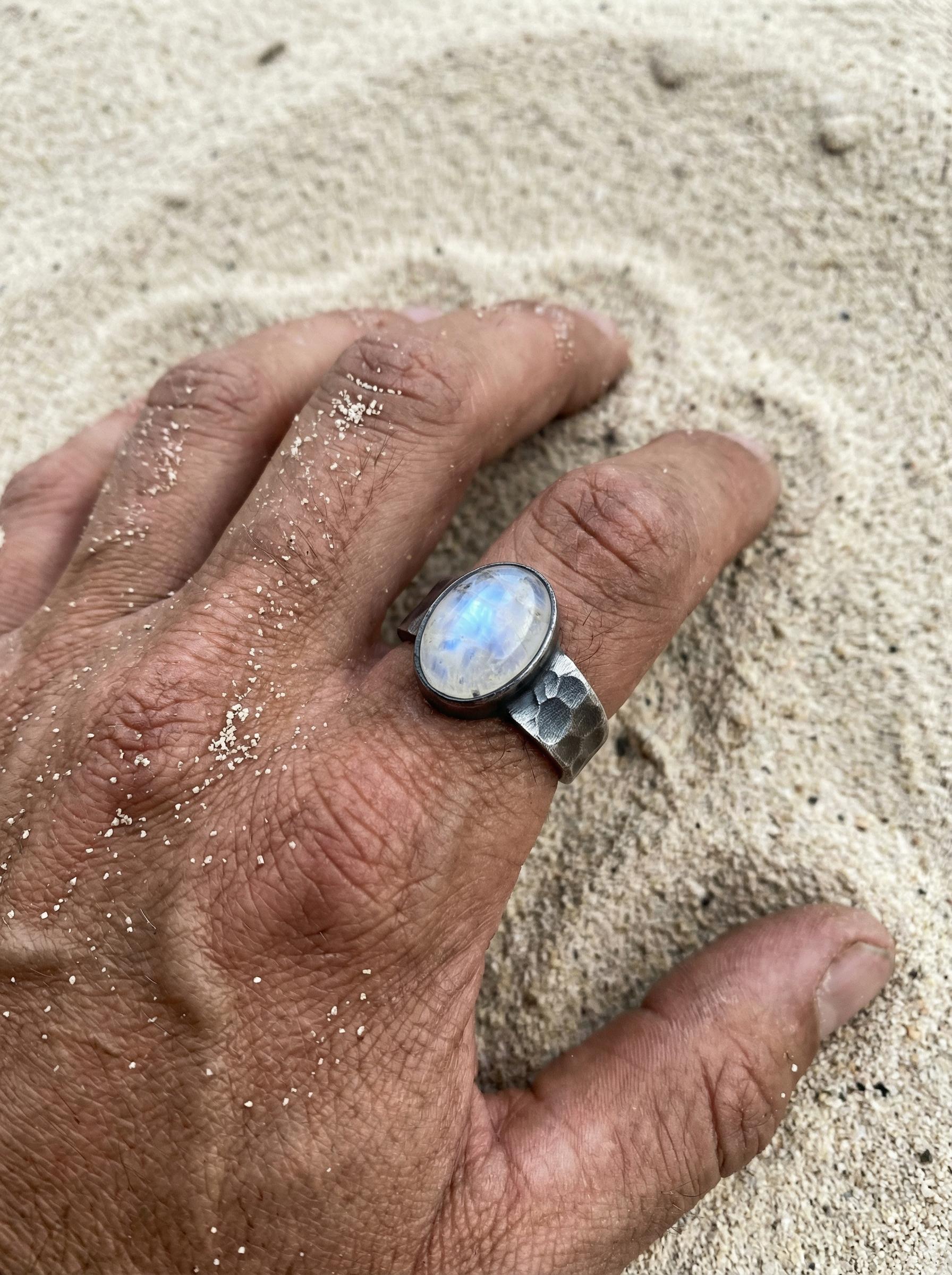 AAA Blue Moonstone men’s ring in oxidized 925 sterling silver shown worn on the hand with wide hammered band.
