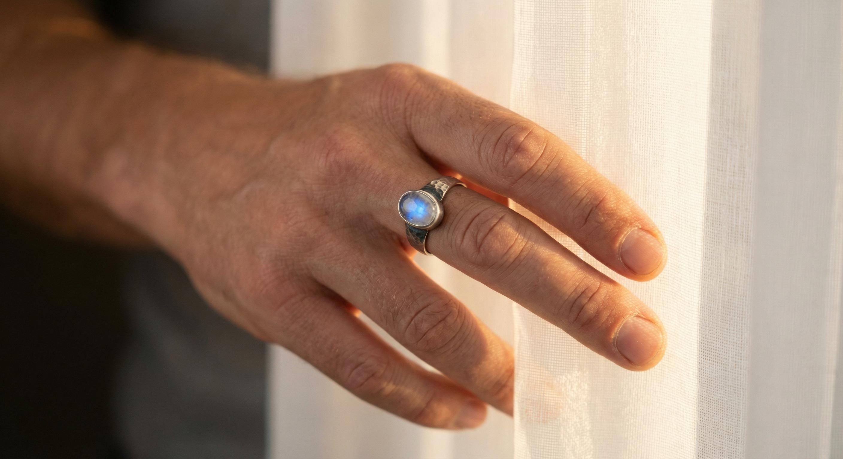 Blue Moonstone ring shown worn on the hand outdoors, with luminous oval gemstone and oxidized hammered silver.