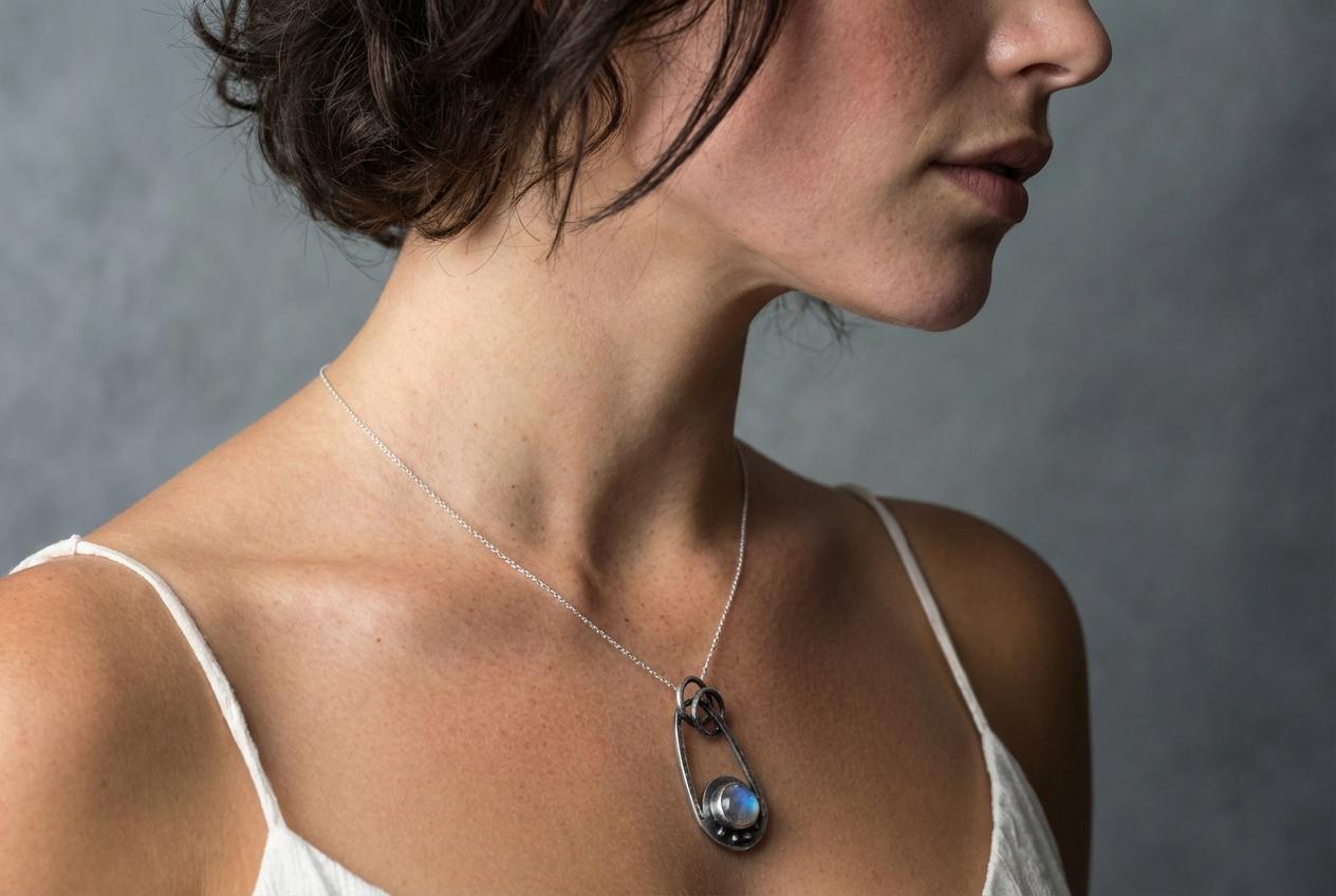 Moonstone sterling silver pendant shown worn on a model, with soft lunar stone glow and small celestial silver design.