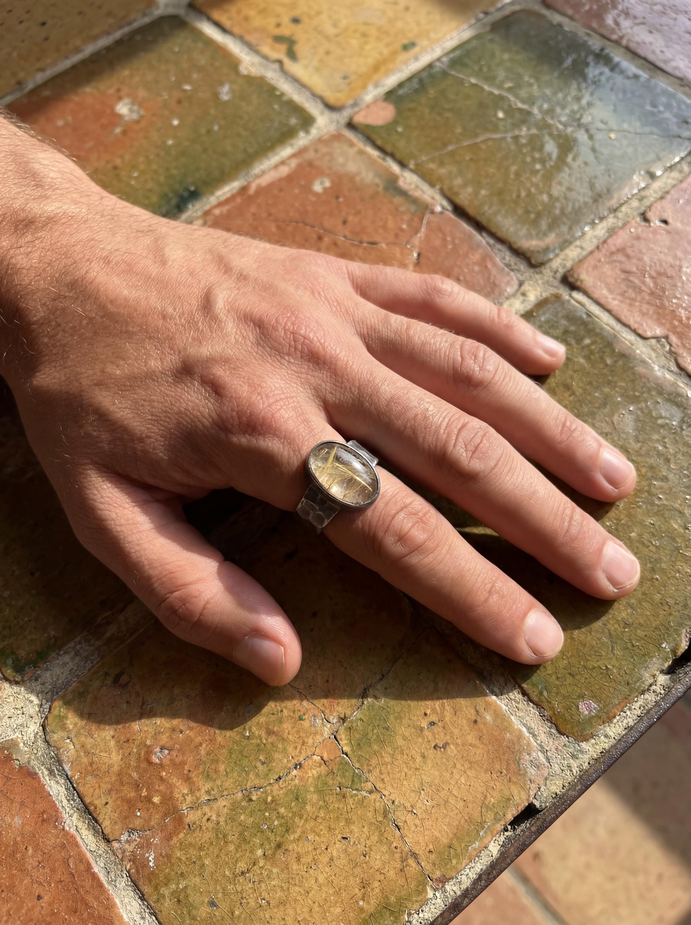 Gold Rutilated Clear Quartz ring shown on the hand, highlighting the oval cabochon and oxidized hammered silver texture.