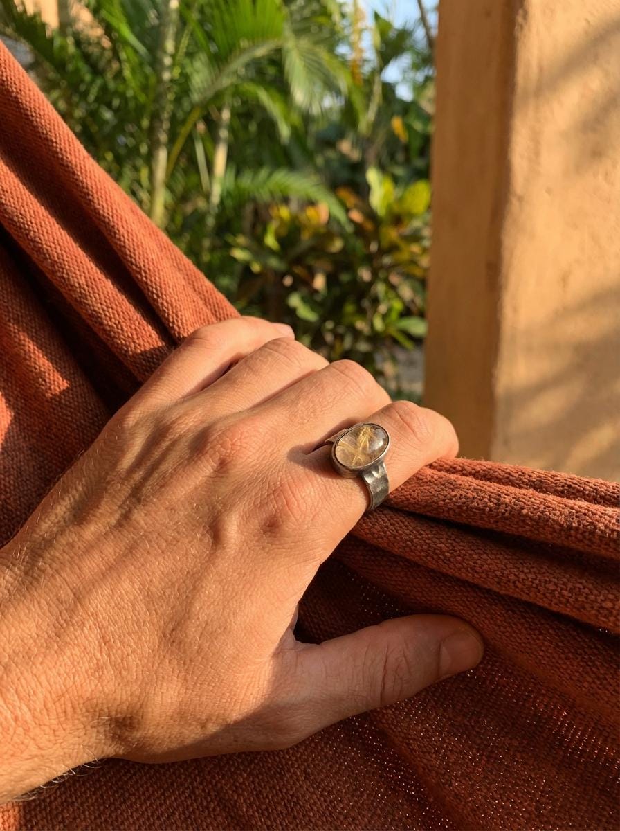 Gold Rutilated Clear Quartz ring shown worn outdoors, with golden internal threads and rugged oxidized sterling silver.