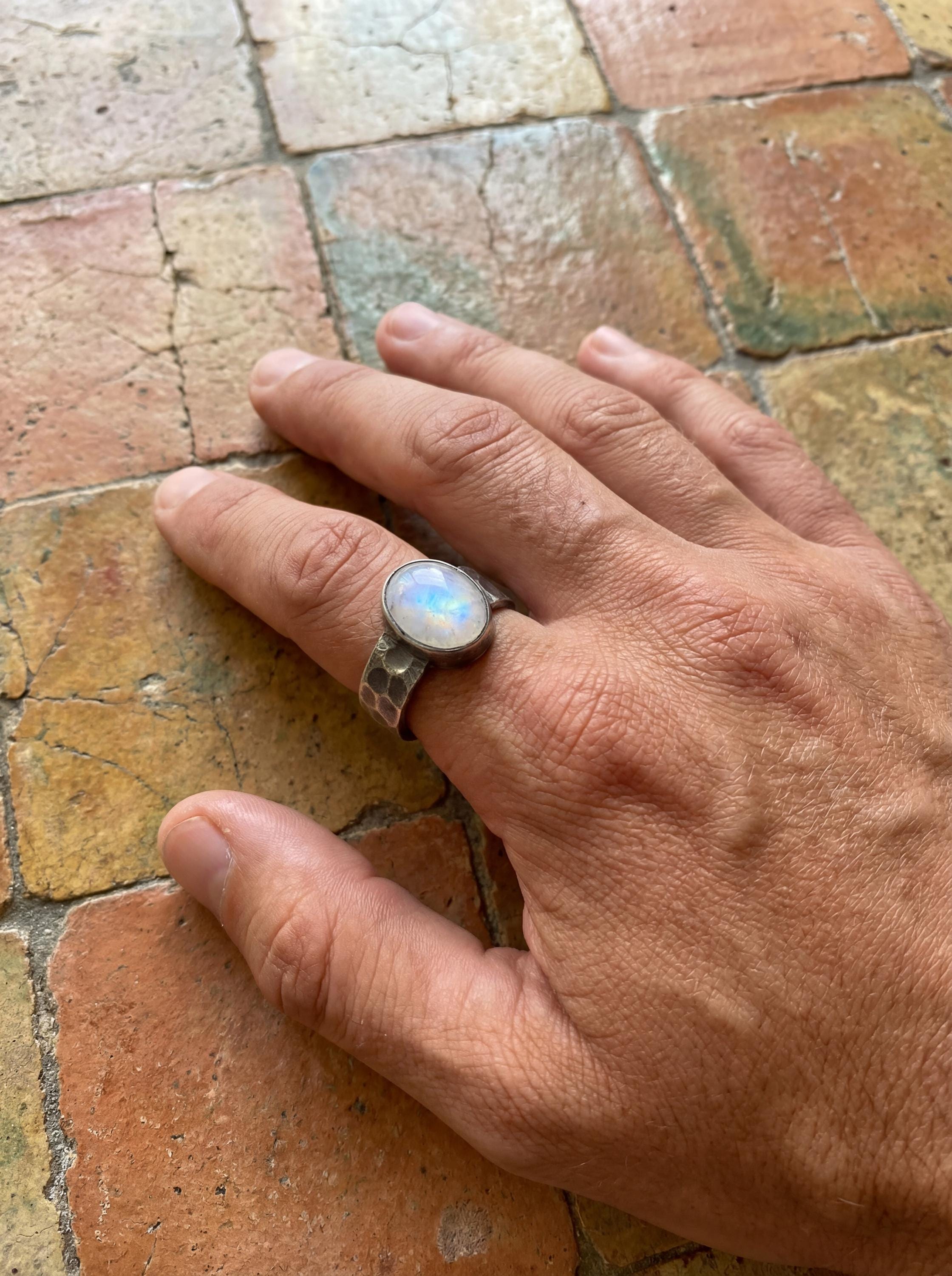 AAA Blue Moonstone ring shown worn outdoors, with pale lunar gemstone glow and rugged hammered silver band.