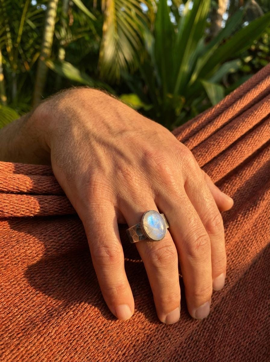 AAA Blue Moonstone men’s ring in oxidized 925 sterling silver shown worn on the hand with hammered silver band.