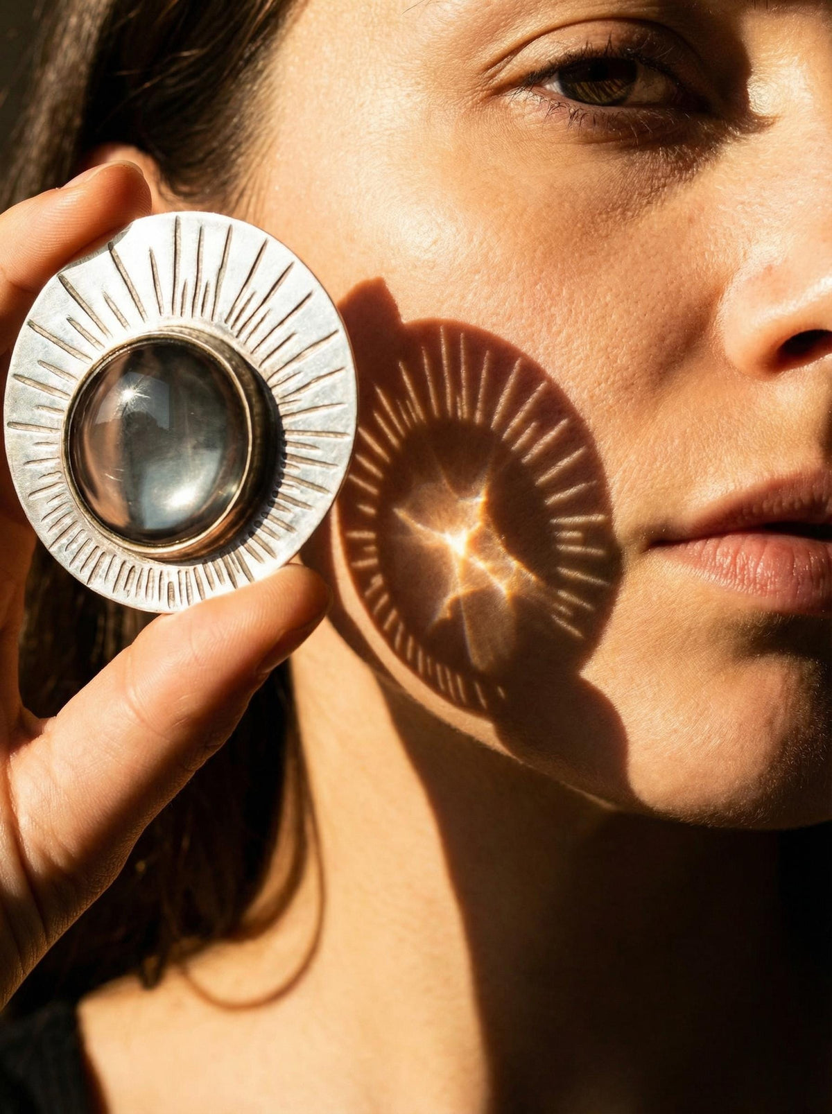 Sun Motif 5x Magnifying Glass pendant held near face with oxidized sterling silver rays casting light.