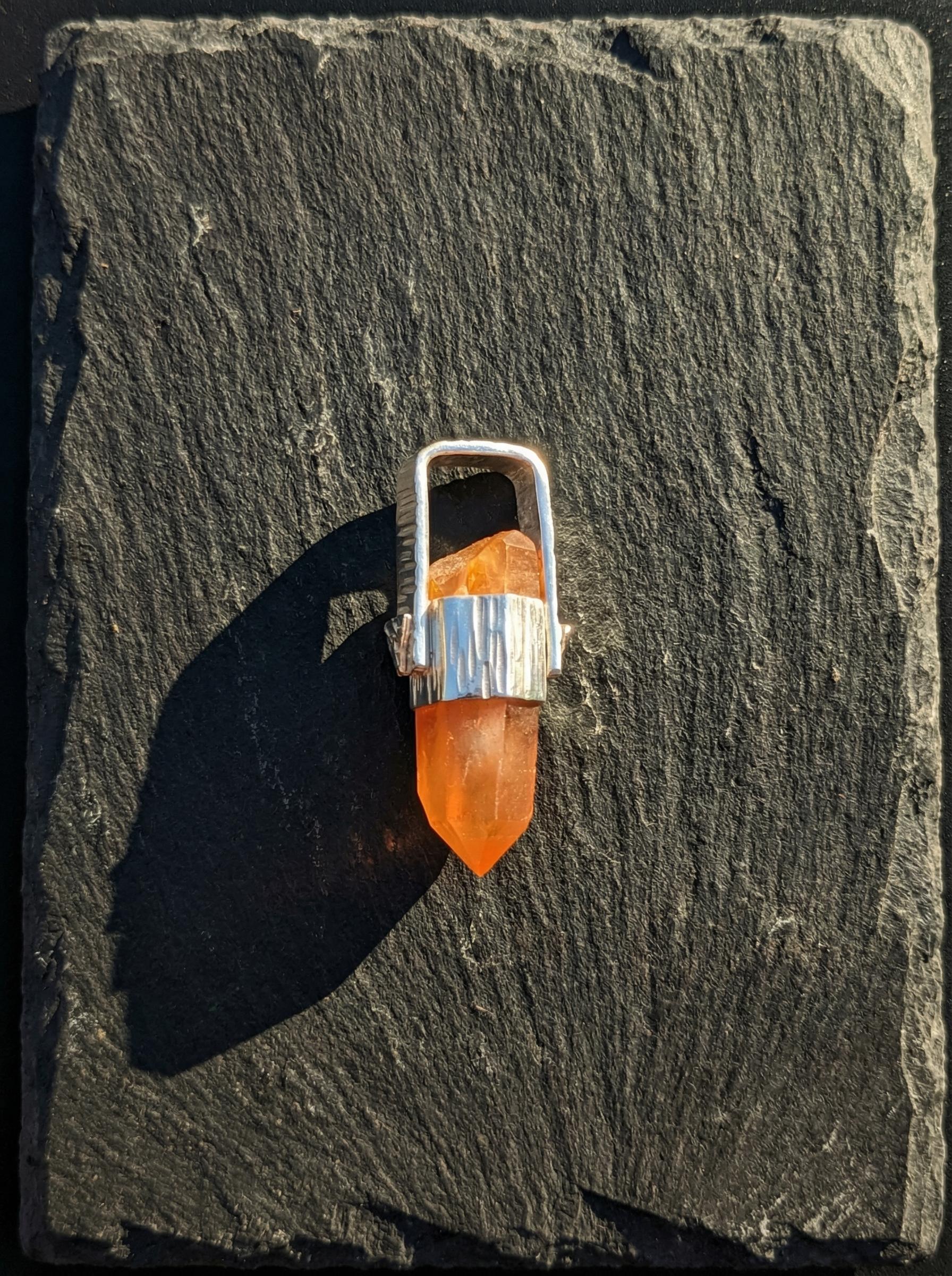 Australian Orange Lithium Lemurian Quartz pendant displayed on slate, with high-shine sterling silver and warm crystal point.