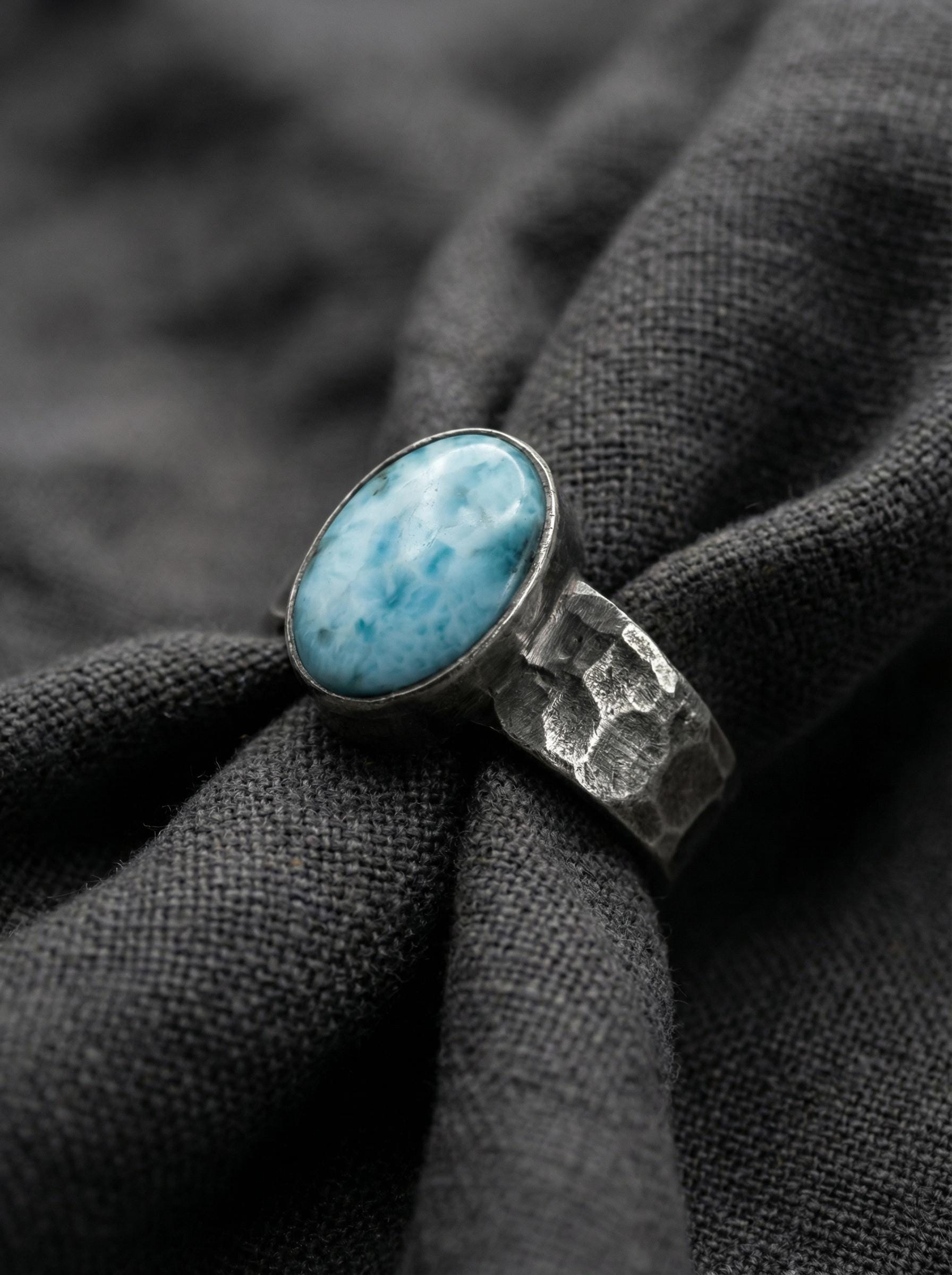 Larimar oval cabochon ring displayed on dark fabric with oxidized hammered sterling silver.
