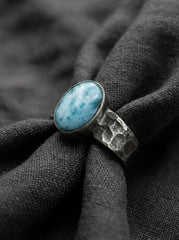 Larimar oval cabochon ring displayed on dark fabric with oxidized hammered sterling silver.