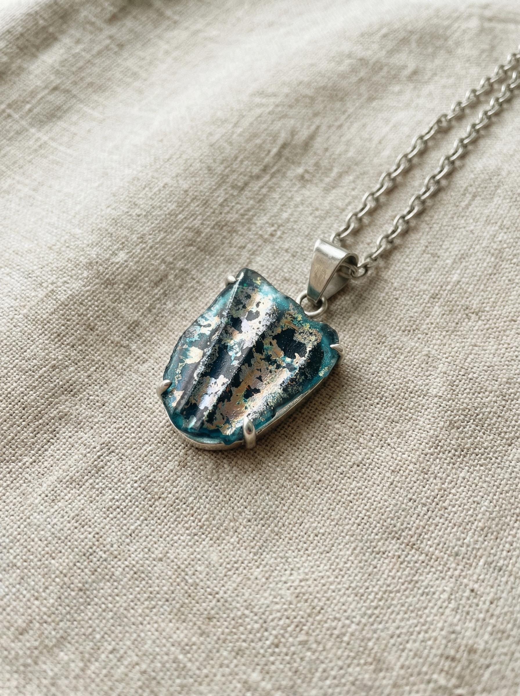 Ancient opalized glass pendant shown on linen with chain and natural relic-like colour pattern.