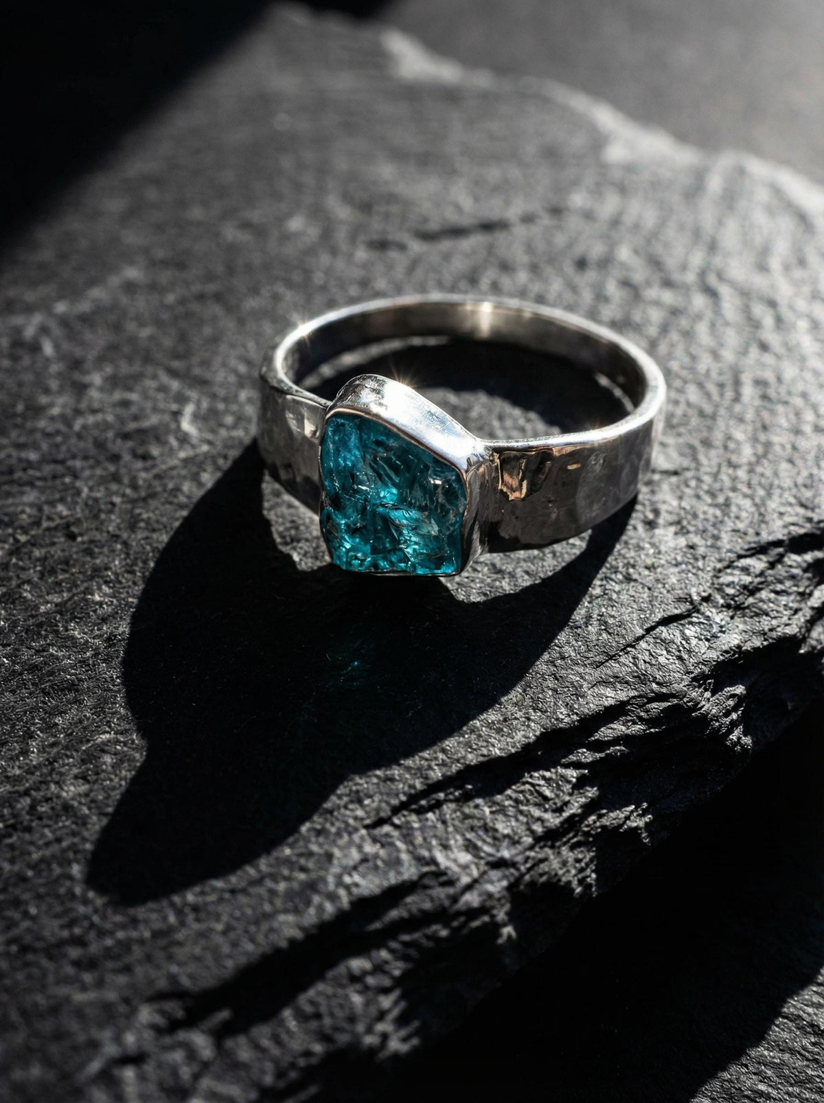 Blue Apatite Textured Silver Ring shown on dark rock with semi rough blue crystal and handmade sterling silver band.