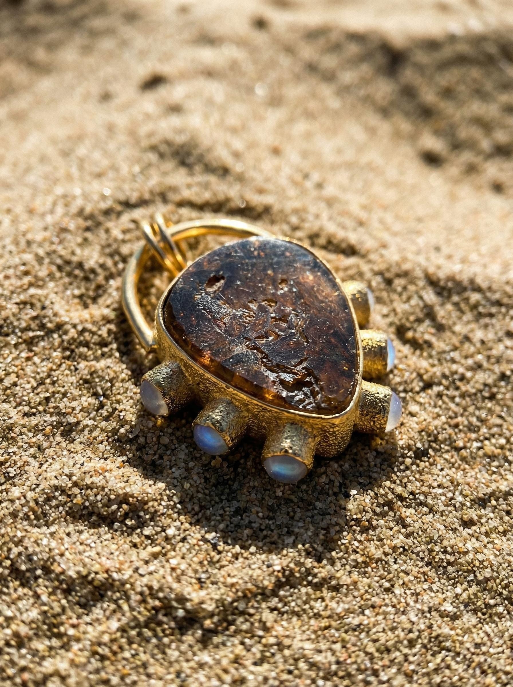 Brown Dravite Tourmaline Moonstone pendant shown on natural sand texture, with 18k gold-plated sterling silver setting.