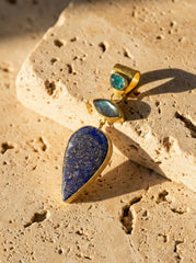 Apatite Labradorite Lapis Lazuli pendant shown on sand, with 18k gold-plated sterling silver and deep blue gemstone design.