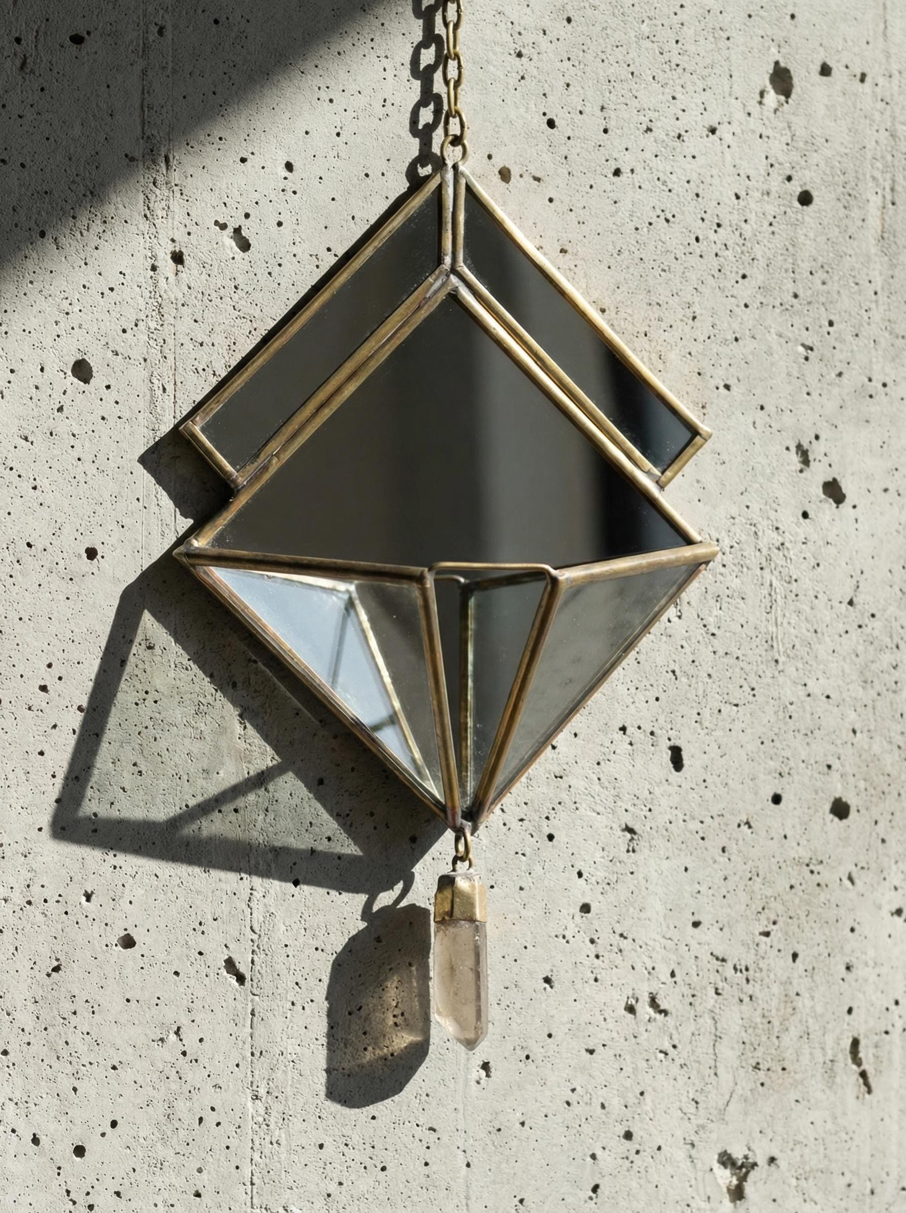 Close-up of geometric brass mirror hanging showing soldered frame detail and raw Clear Quartz point.