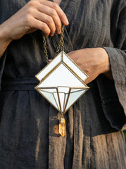 Quartz Reliquary Geometric Mirror Hanging shown held by a model, with brass frame and raw Quartz point.