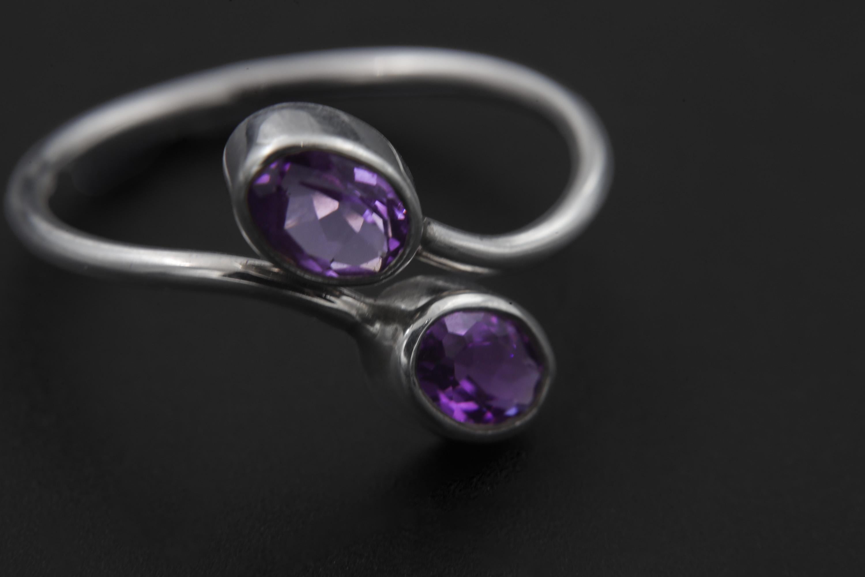 Close view of two faceted Amethyst stones set in polished sterling silver bezels.