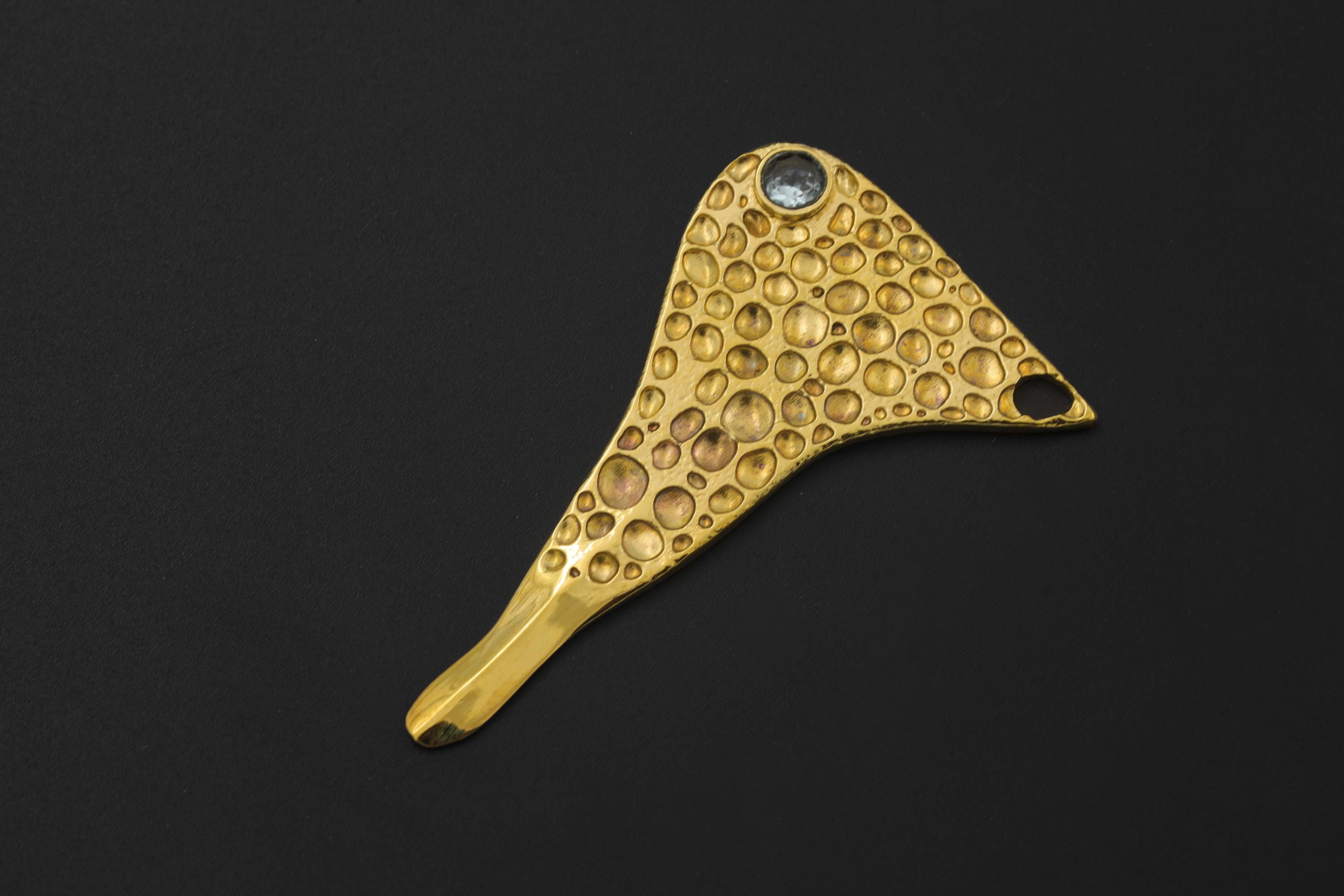 Golden Ritual Blue Topaz spoon pendant shown on dark background with abstract bubble texture and side-set gemstone.