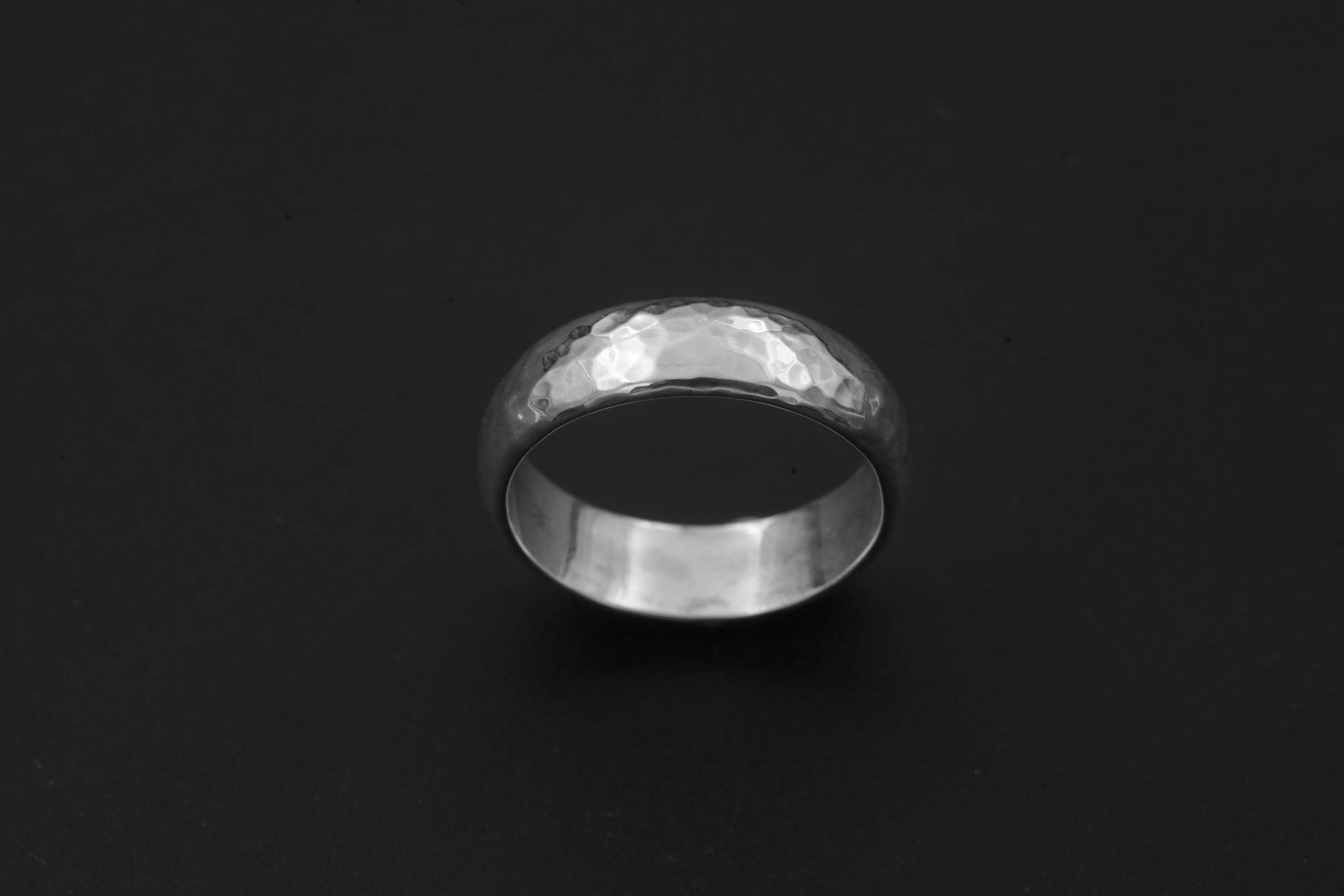 Sterling silver hammered band displayed on dark background with simple polished ring profile.