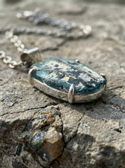 Raw Afghani ancient opalized glass pendant displayed on rock with sterling silver chain.