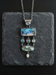Ocean’s Symphony pendant shown on slate with seven gemstones, oxidized sterling silver, and layered ocean-inspired statement design.