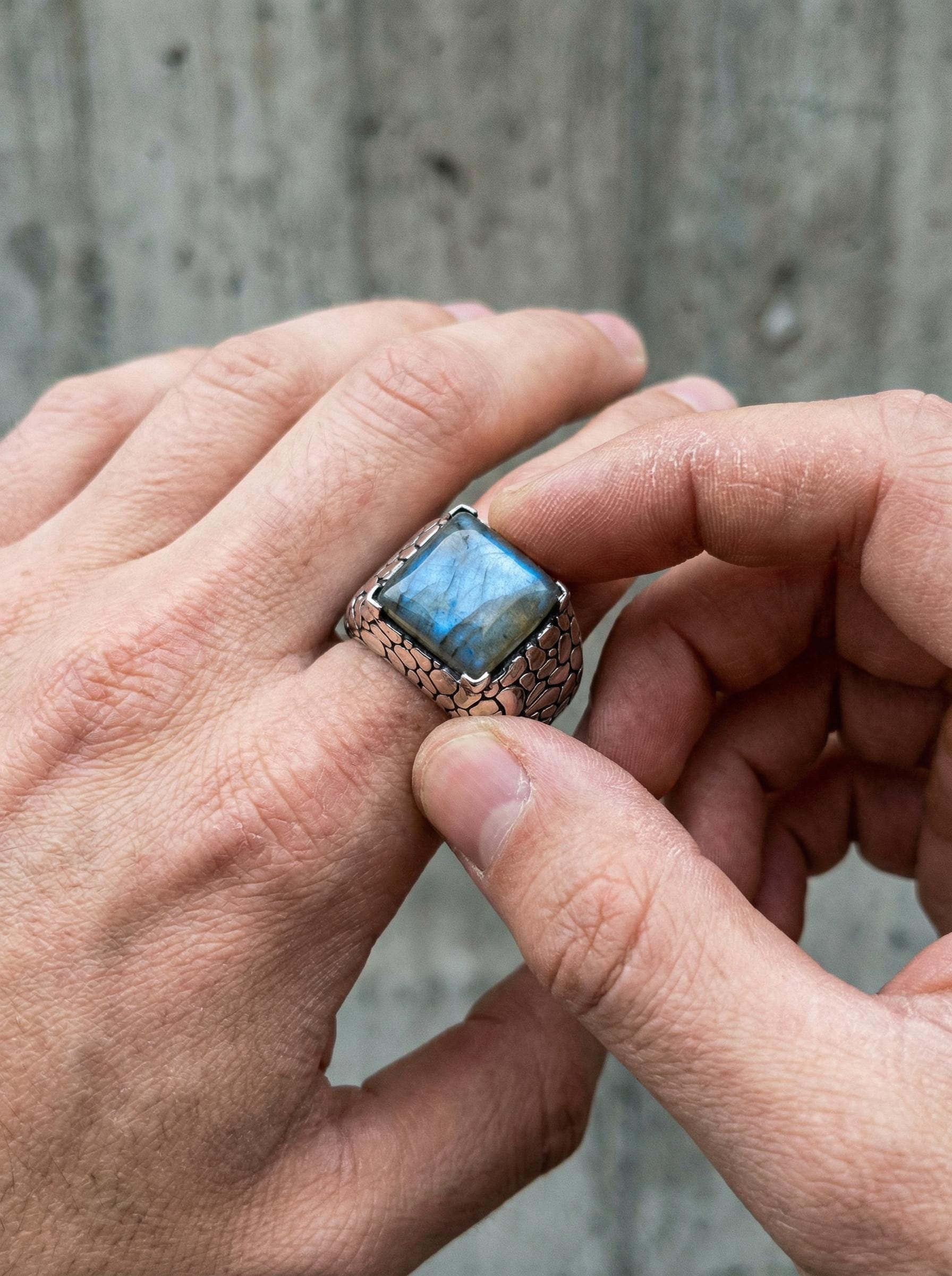 Labradorite ring shown held in hand with wide textured sterling silver band and blue flash stone.