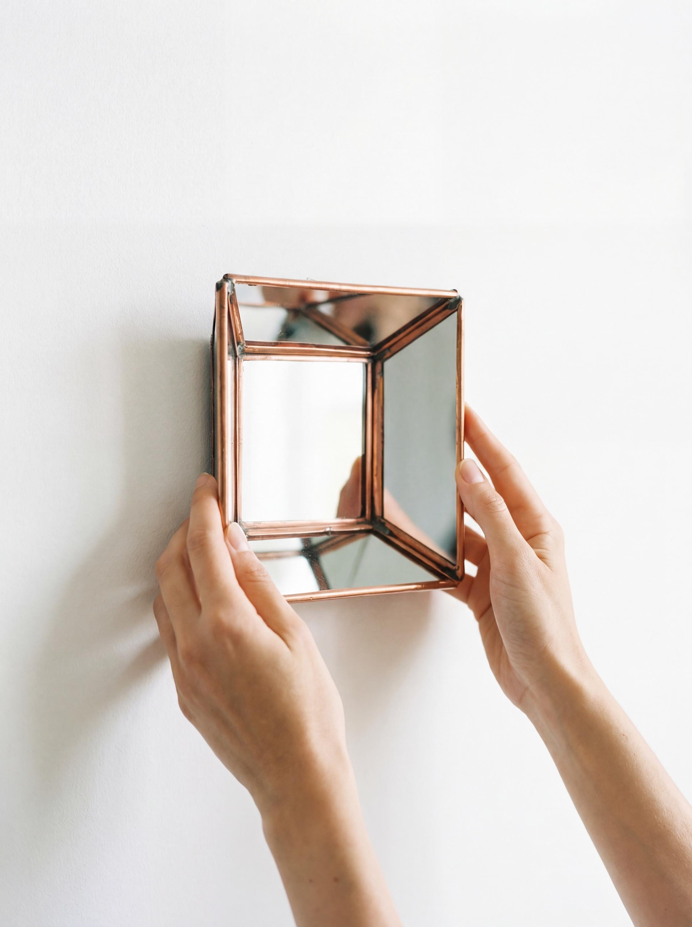Handheld square copper mirror showing geometric angled mirror panels and handmade copper construction.