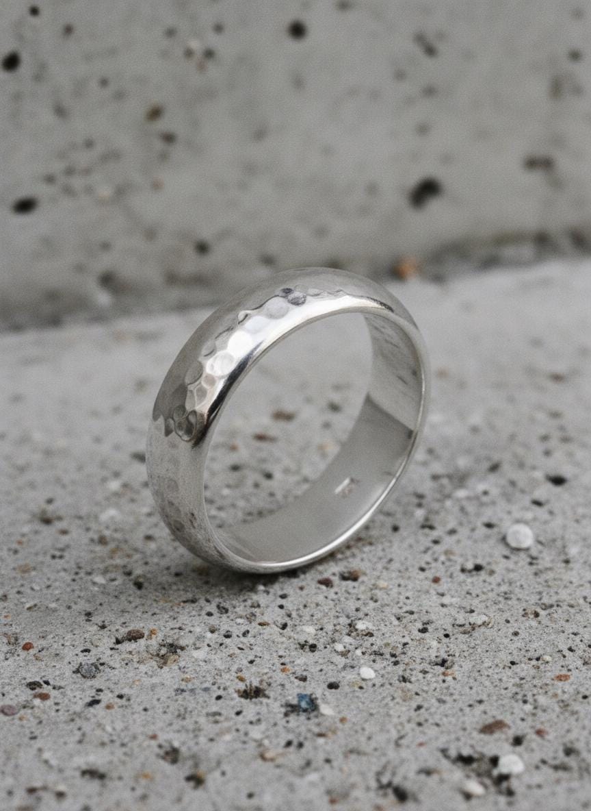 Hammered silver band standing on concrete surface showing textured handmade finish.