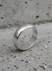 Hammered silver band standing on concrete surface showing textured handmade finish.