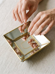 Brass mirror geometric tray used as a jewelry display dish with rings placed inside the reflective square base.