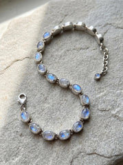 Blue Moonstone bracelet displayed on fabric with oval cabochon stones and adjustable sterling silver chain.