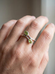 Peridot sterling silver wrap ring shown worn on hand with two oval green gemstones.
