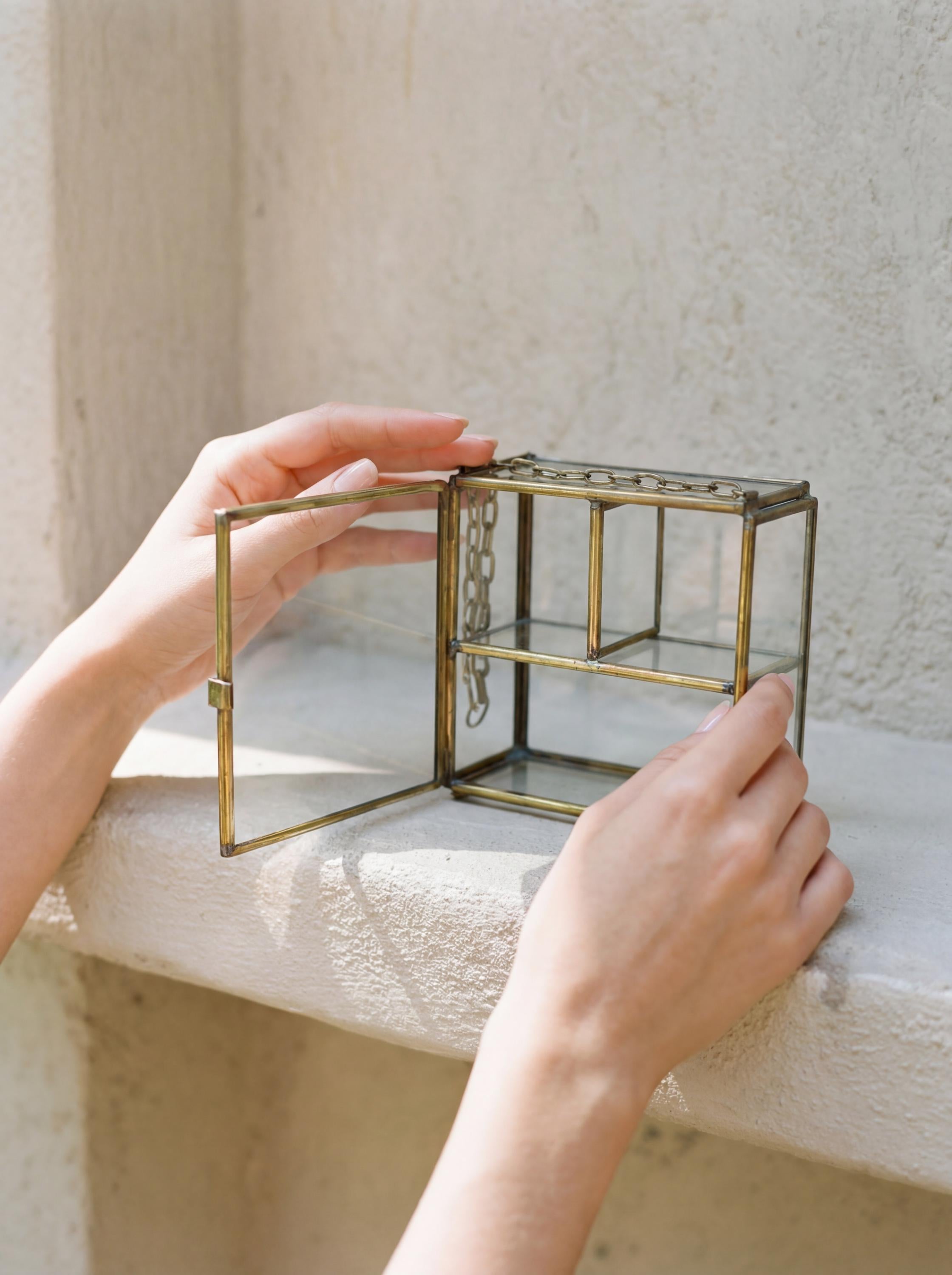 Hands opening large brass and glass display box, showing hinged door and internal shelf for jewelry or crystals.