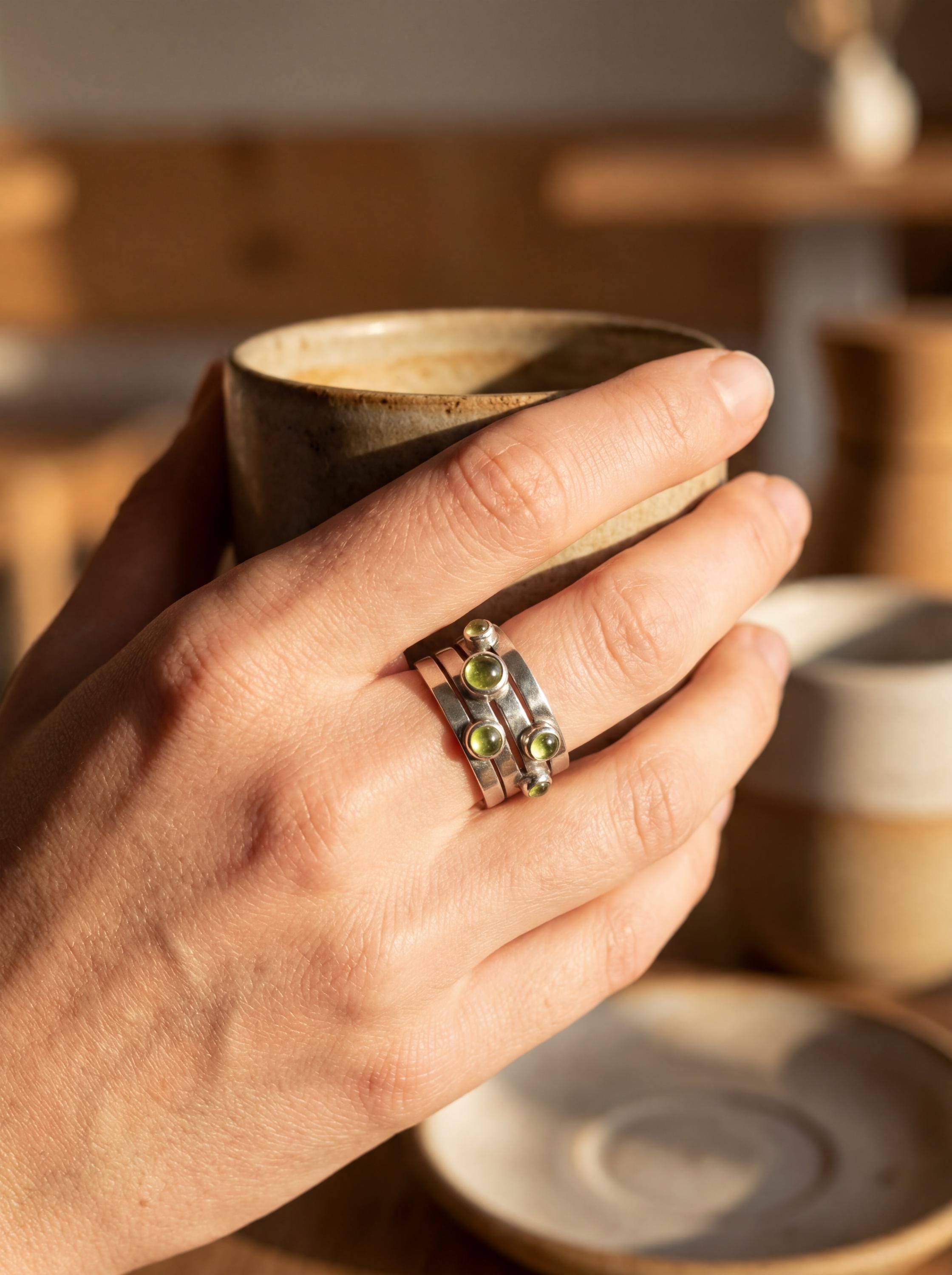 Five Stone Peridot ring shown worn while holding cup with polished silver and olive green stones.