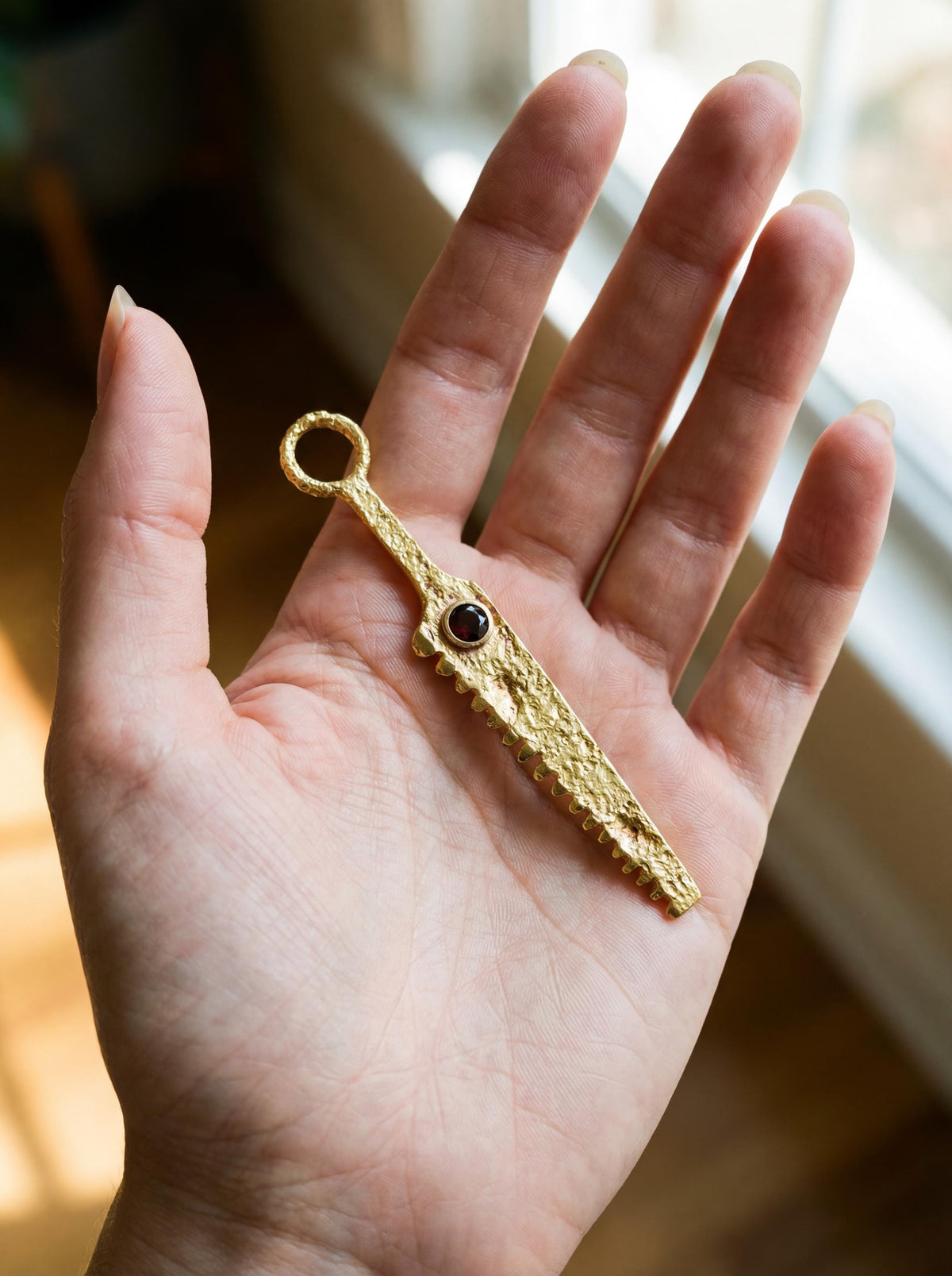 Gold-plated Garnet cutter spoon pendant held in hand as a functional ritual talisman.