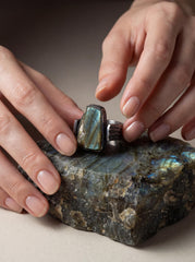 Raw Labradorite sterling silver ring shown held on stone with green-blue flash and rugged textured band.