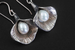 Pearl drop earrings shown held near stone with polished sterling silver and ocean bloom design.