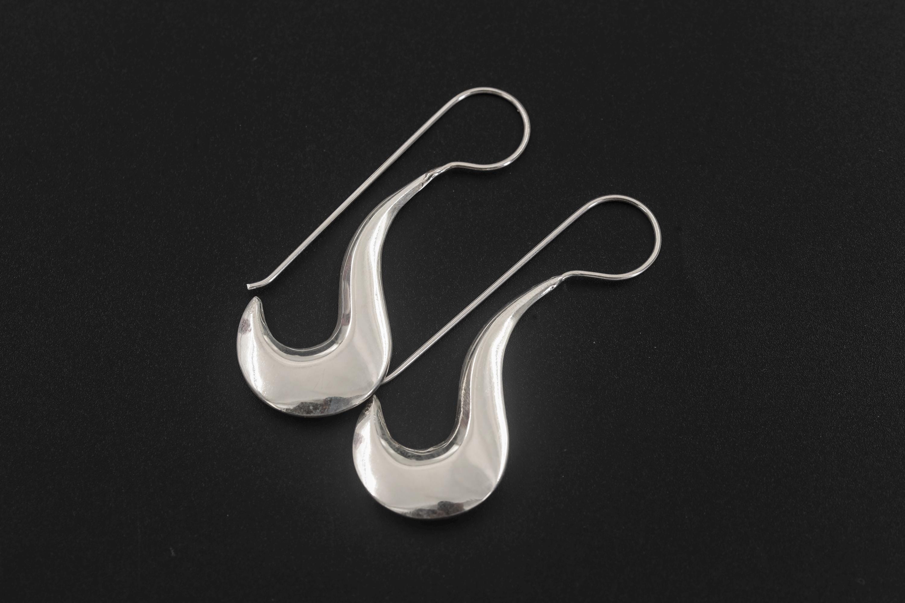 Sterling silver crescent drop earrings shown on dark slate with sculptural silver shine.