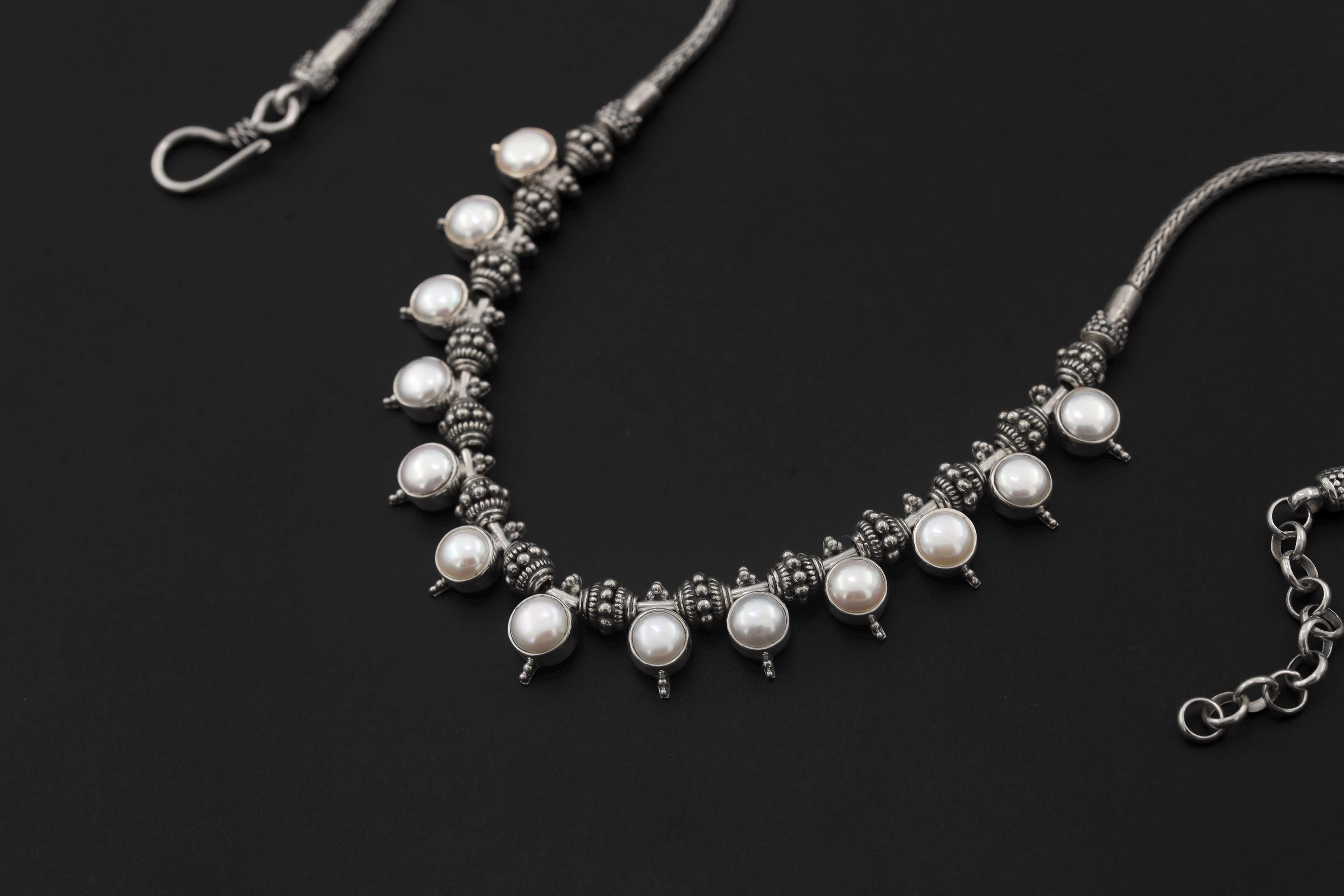Pearl necklace shown on sand with natural white Pearls and detailed sterling silver bead elements.