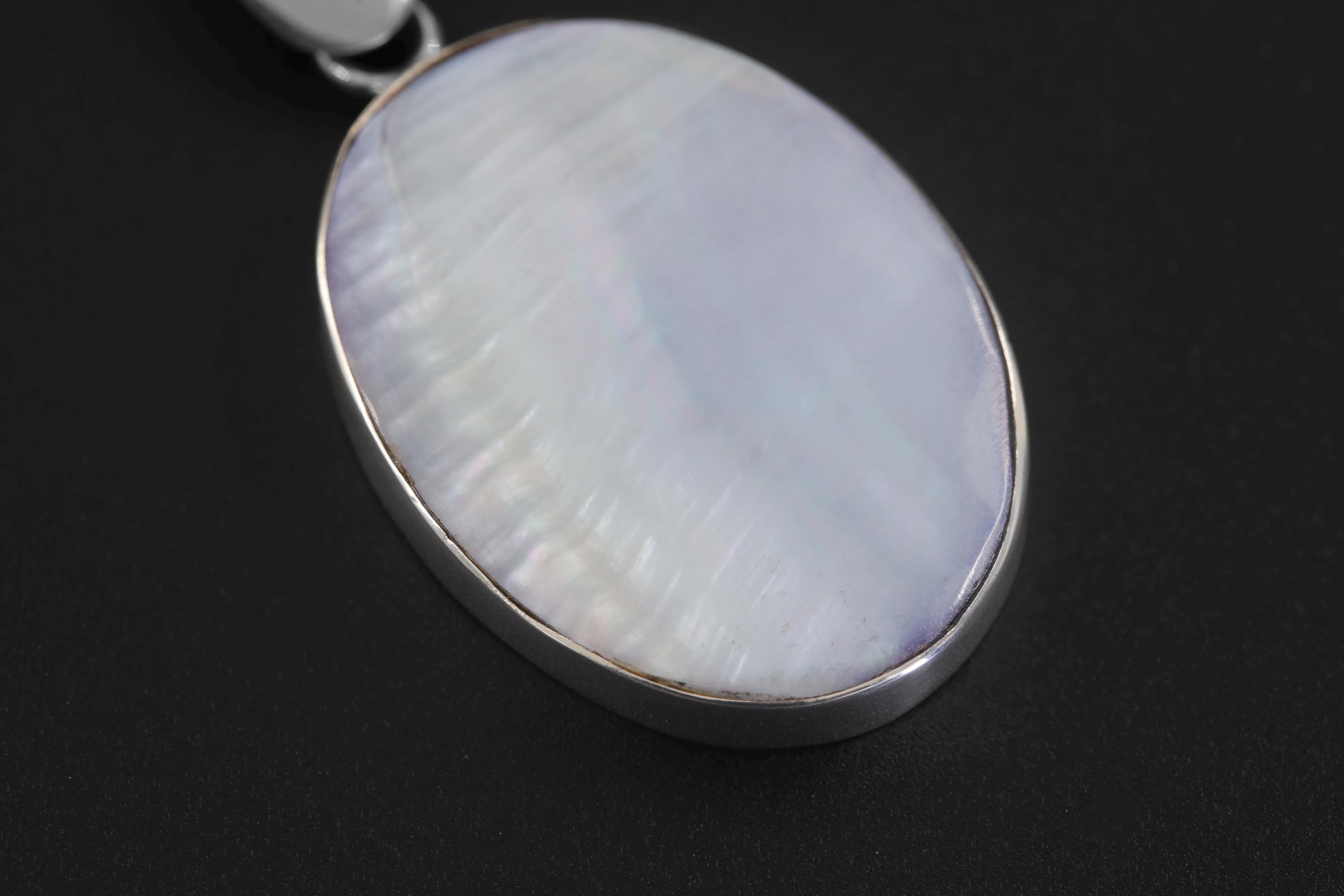 Mother of Pearl oval pendant displayed on dark background with smooth polished sterling silver bezel.
