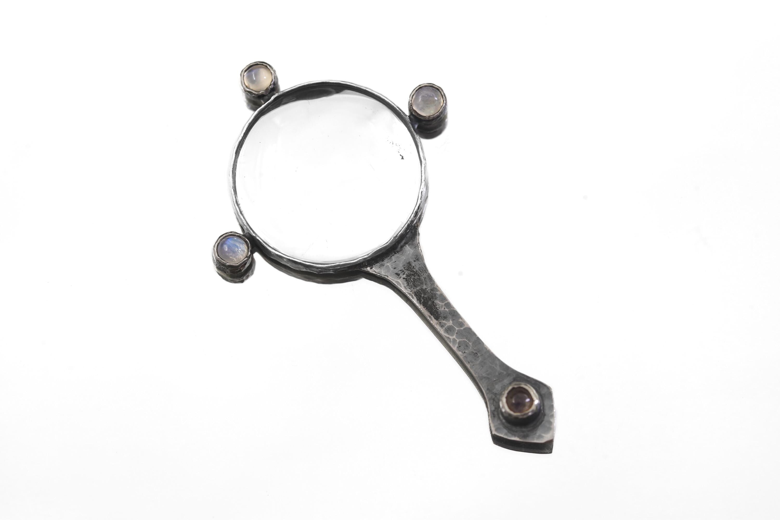 Moonstone magnifier pendant displayed on white background with hammered oxidized silver handle and glass lens.